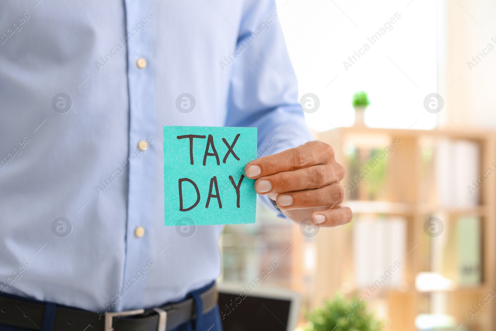 Photo of Man holding card with words TAX DAY indoors