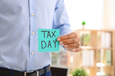 Photo of Man holding card with words TAX DAY indoors