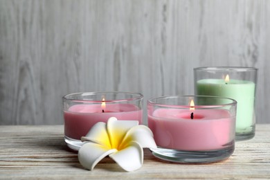 Photo of Burning candles and plumeria flower on white wooden table