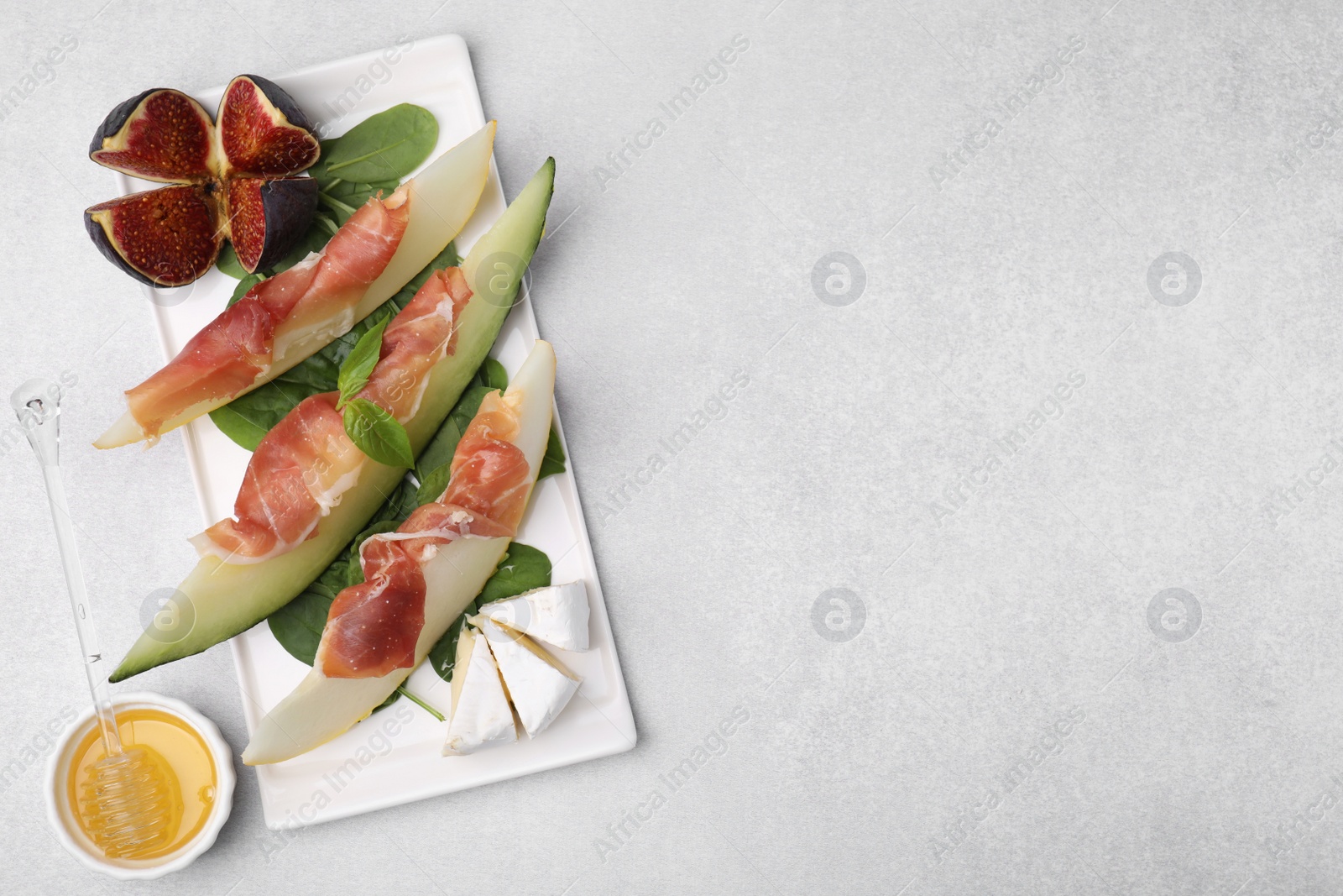 Photo of Tasty melon, jamon and figs served on light grey table, flat lay. Space for text