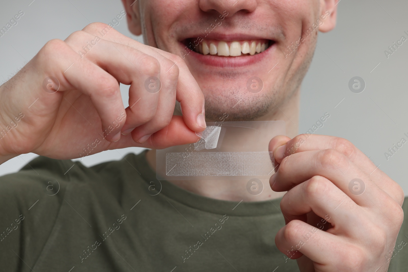 Photo of Young man with whitening strips on light grey background, closeup