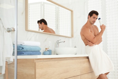 Handsome young man with deodorant in bathroom