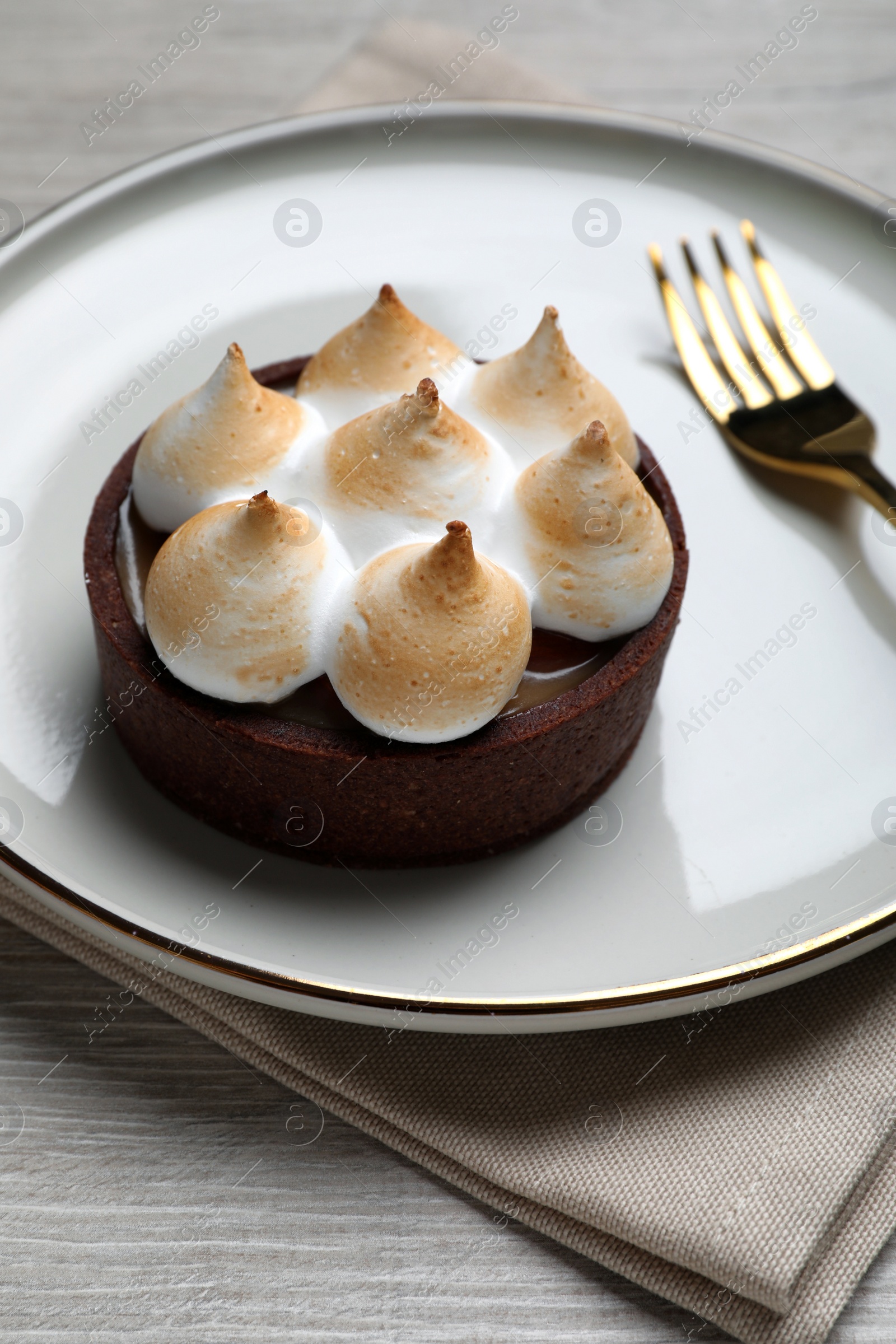 Photo of Delicious salted caramel chocolate tart with meringue served on light beige wooden table, closeup