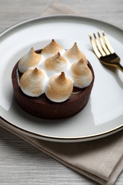 Photo of Delicious salted caramel chocolate tart with meringue served on light beige wooden table, closeup