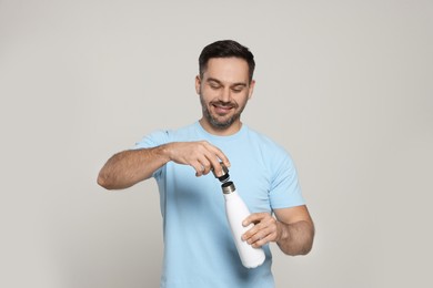 Happy man opening thermo bottle on light grey background