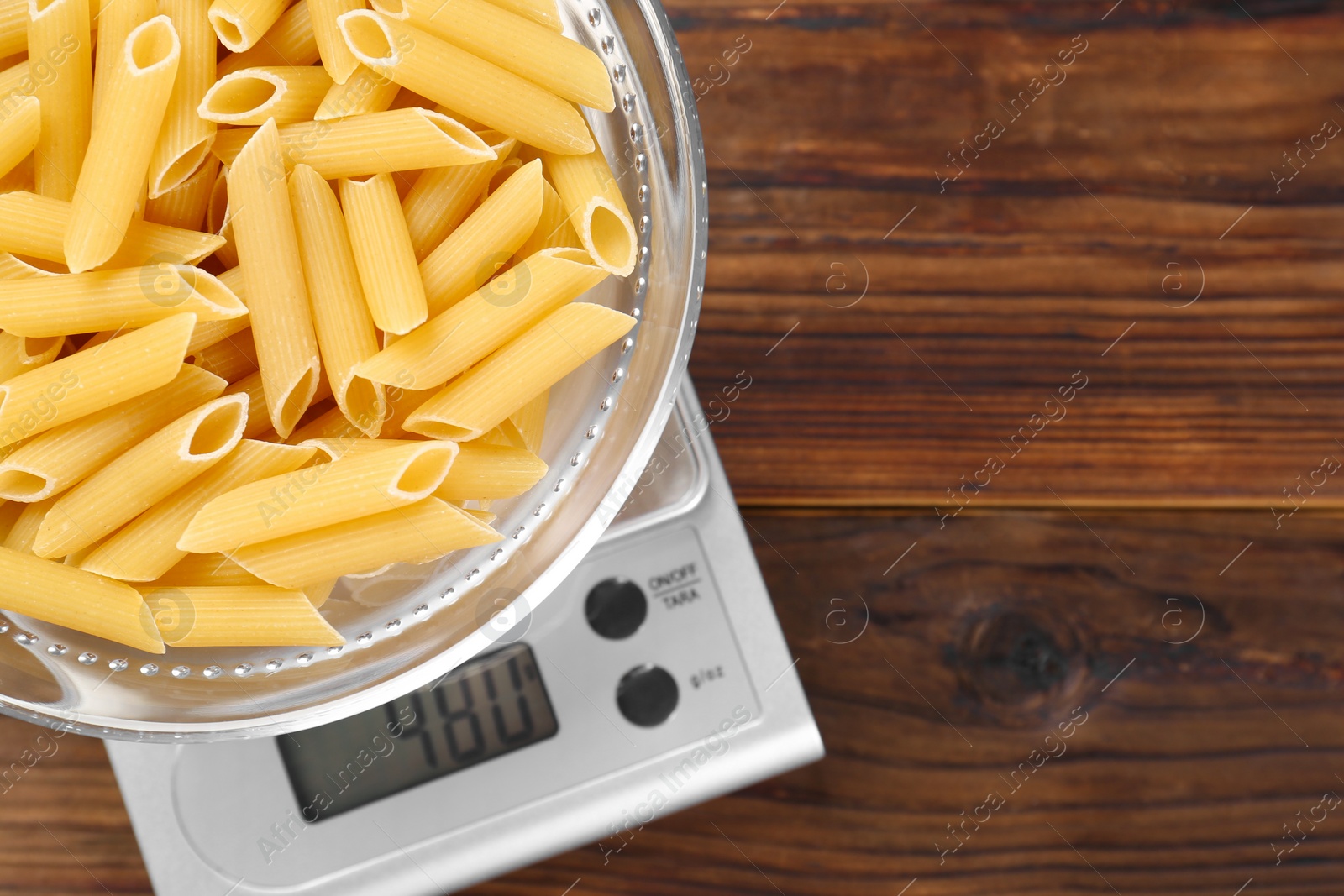 Photo of Kitchen scale with bowl of pasta on wooden table, top view. Space for text