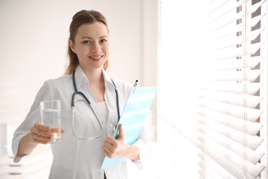Photo of Nutritionist with glass of water and clipboard near window in office. Space for text