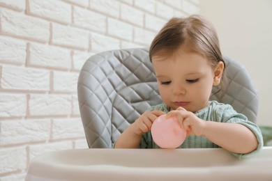 Cute little baby with toy in high chair indoors. Space for text