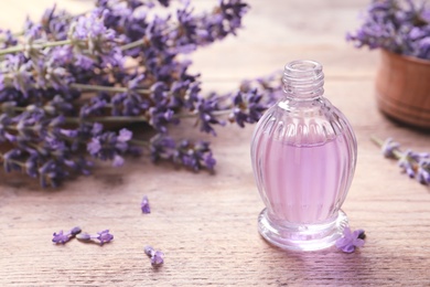 Glass bottle of natural cosmetic oil and lavender flowers on wooden table, space for text