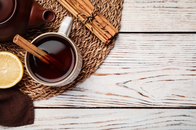 Photo of Delicious hot tea with cinnamon and lemon on white wooden table, flat lay. Space for text