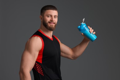 Photo of Young man with muscular body holding shaker of protein on grey background