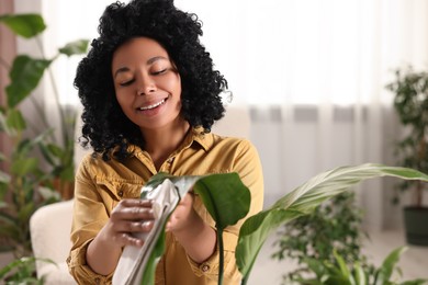 Happy woman wiping beautiful houseplant leaf indoors