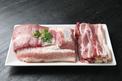 Photo of Pieces of raw pork belly and parsley on black textured table