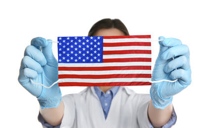 Doctor holding medical mask with USA flag pattern on white background. Dangerous virus