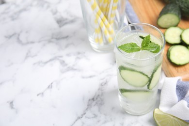 Glass of refreshing cucumber water with mint on white marble table, space for text