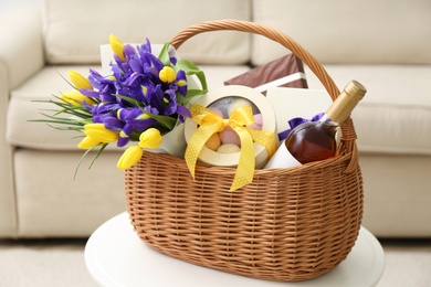 Photo of Wicker basket with gift, bouquet and wine on white table indoors