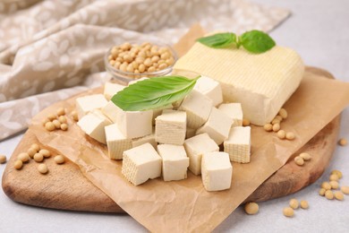 Photo of Delicious tofu cheese, basil and soybeans on light gray table, closeup