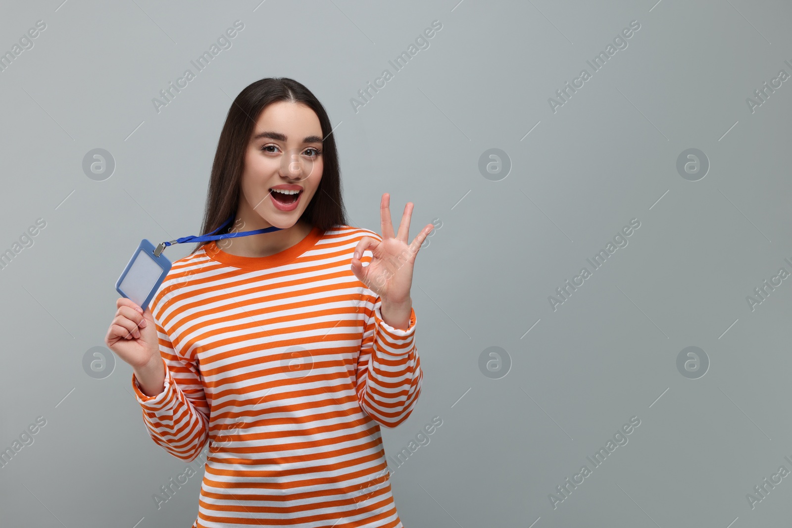 Photo of Excited woman holding vip pass badge and showing ok gesture on grey background. Space for text