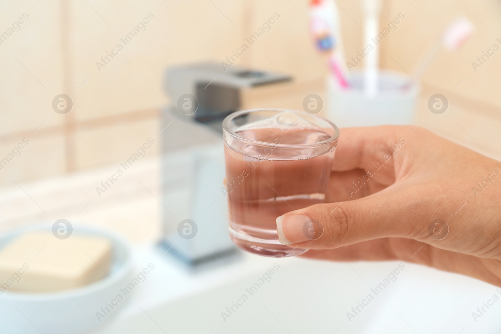 Photo of Woman holding glass with mouthwash for teeth and oral care in bathroom