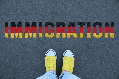 Image of Woman standing on asphalt near word Immigration in colors of flag of Germany, top view