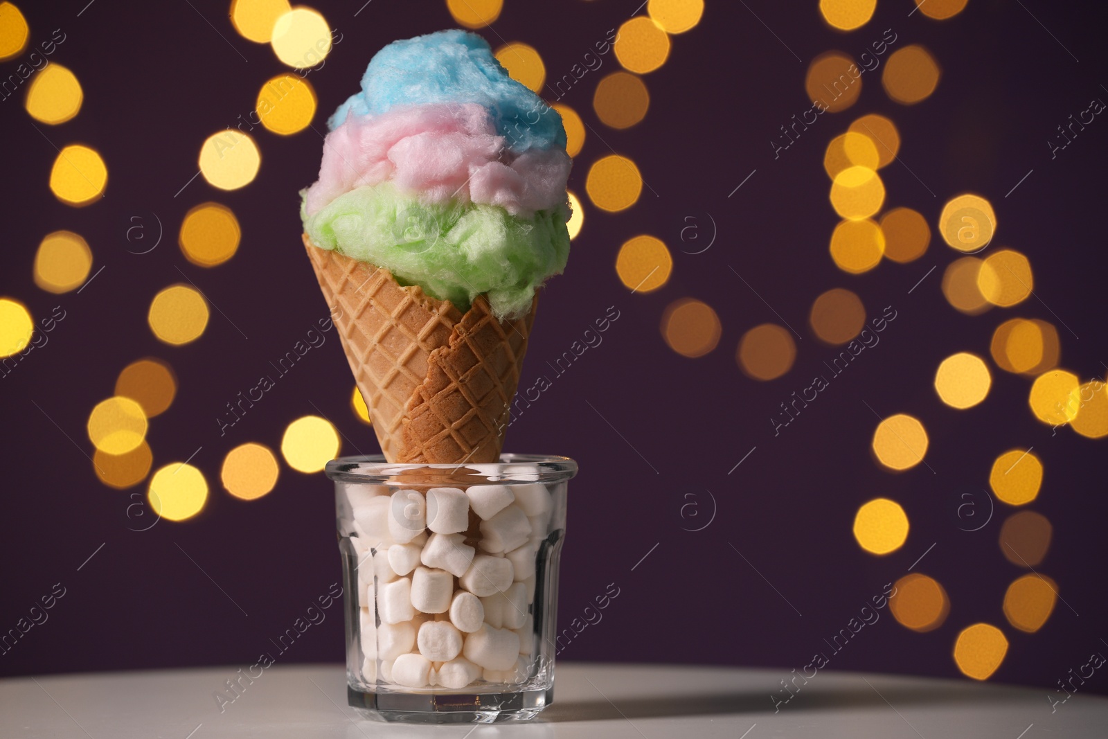 Photo of Sweet cotton candy in waffle cone on table against blurred lights, closeup