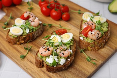 Delicious sandwiches with guacamole, shrimps and microgreens on wooden board, closeup