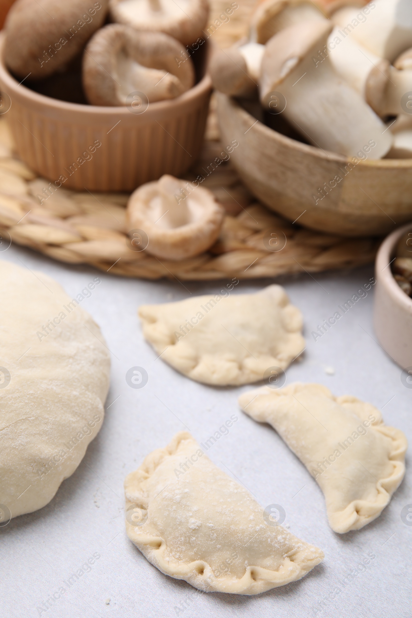 Photo of Process of making dumplings (varenyky) with mushrooms. Raw dough and ingredients on white table, closeup