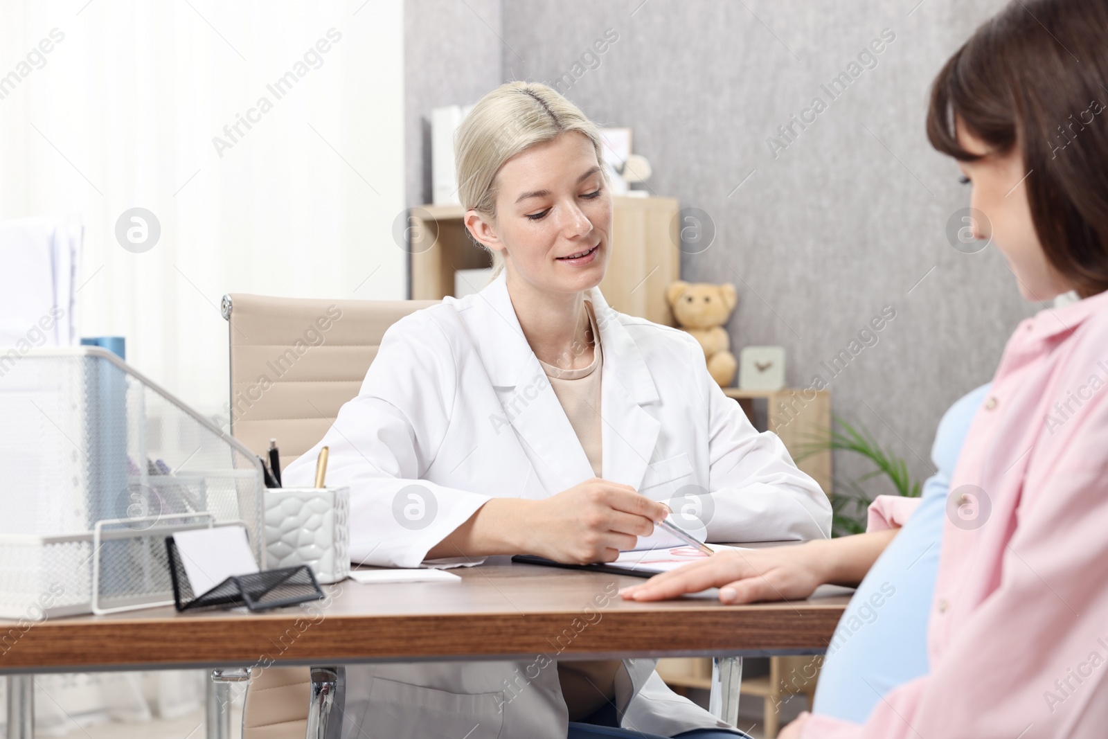 Photo of Doctor consulting pregnant patient at table in clinic