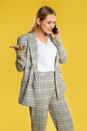 Emotional woman talking on smartphone against yellow background