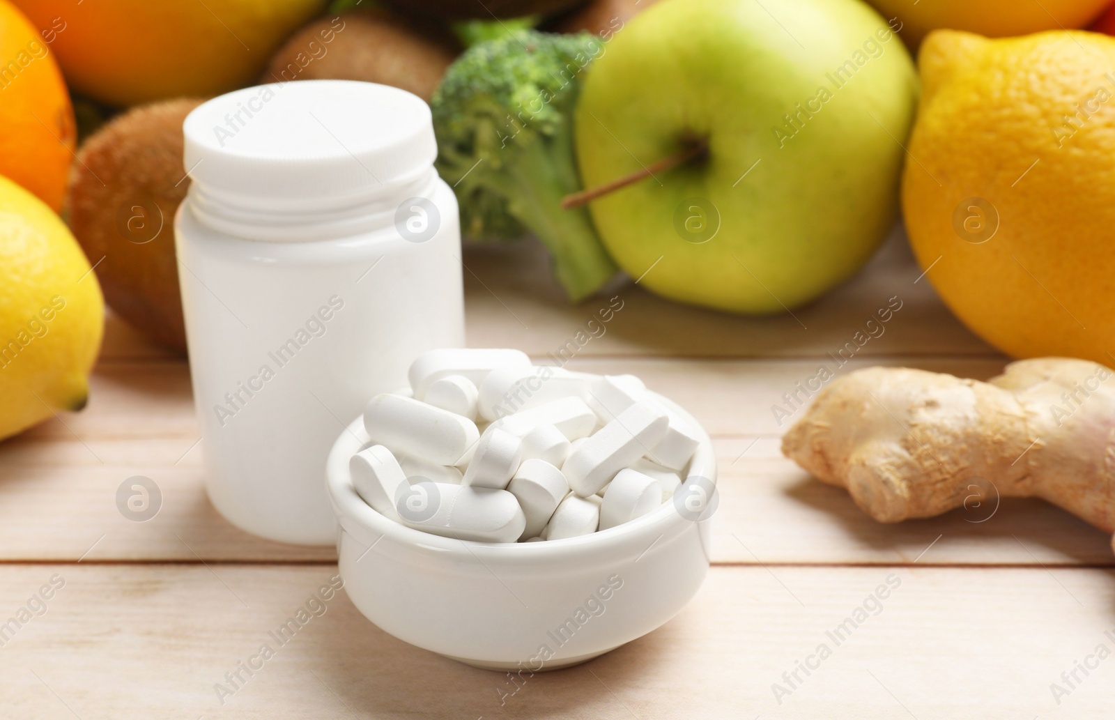 Photo of Dietary supplements. Bottle and bowl with pills near food products on light wooden table, closeup