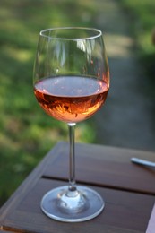 Photo of Glass of rose wine on wooden table in garden