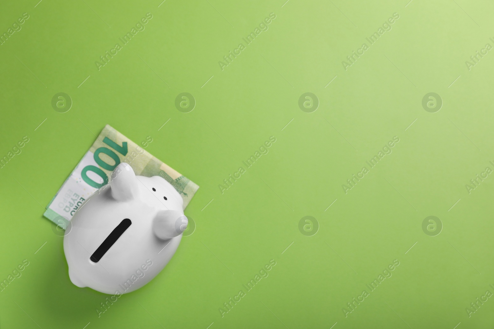 Photo of Ceramic piggy bank and euro banknote on light green background, top view with space for text. Financial savings