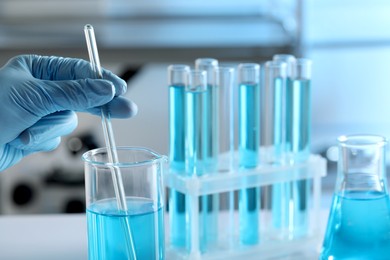Photo of Scientist taking sample of light blue liquid in laboratory, closeup