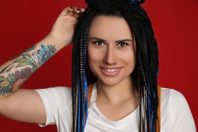 Photo of Beautiful young woman with nose piercing and dreadlocks on red background