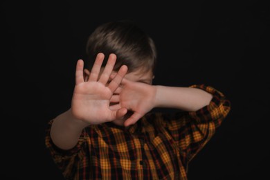 Boy making stop gesture against black background, focus on hands. Children's bullying