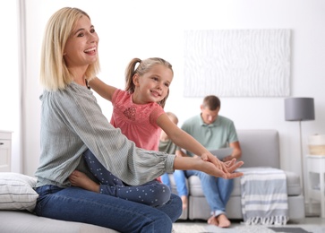 Photo of Happy mother playing with her daughter while father and son using laptop at home