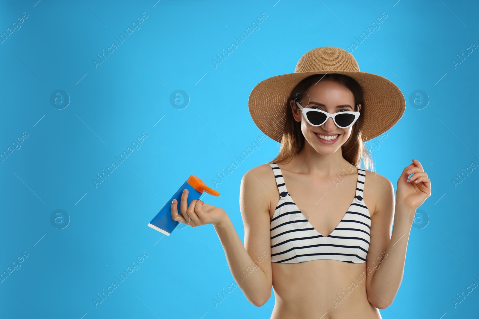 Photo of Young woman with sun protection cream on light blue background. Space for text