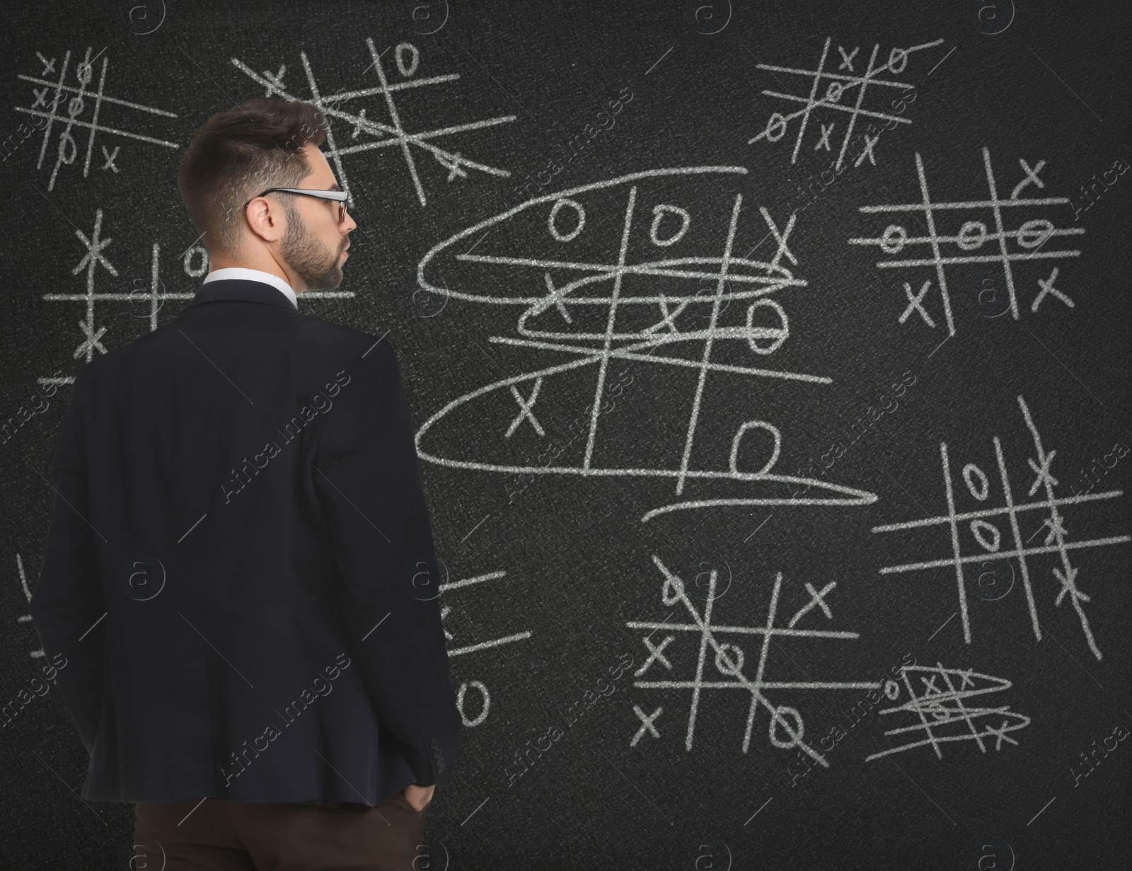 Image of Young businessman in elegant suit near blackboard with drawn tic tac toe game 