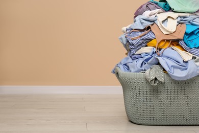 Photo of Laundry basket with clothes near beige wall indoors. Space for text