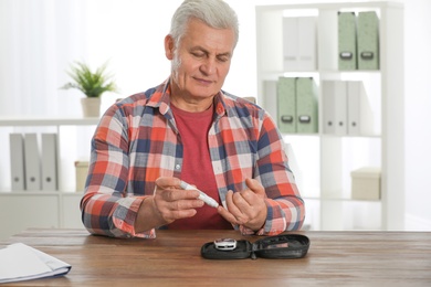 Senior man using lancet pen at table. Diabetes control