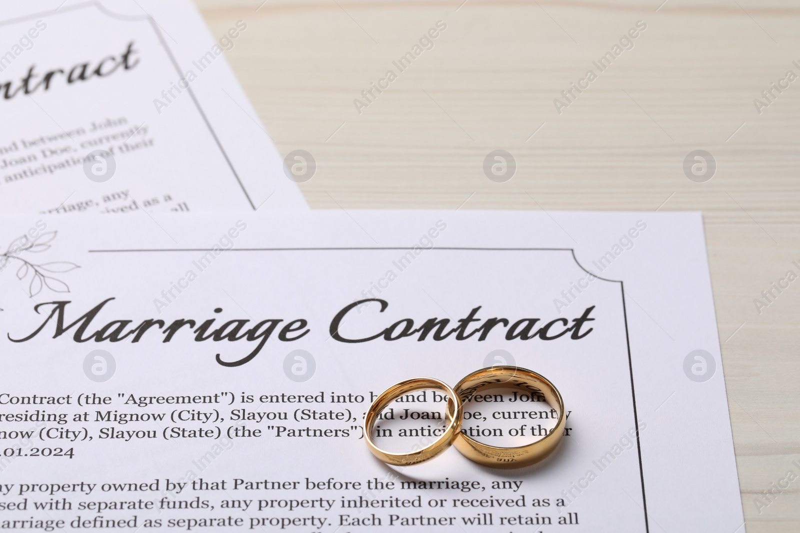 Photo of Marriage contracts and gold rings on light wooden table, closeup