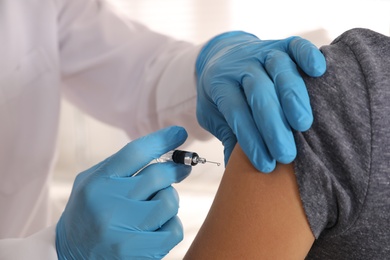 Doctor vaccinating young woman against Covid-19 in clinic, closeup