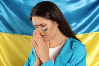 Sad young woman with clasped hands near Ukrainian flag