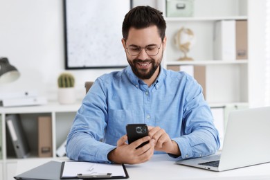 Photo of Happy young man using smartphone at white table in office