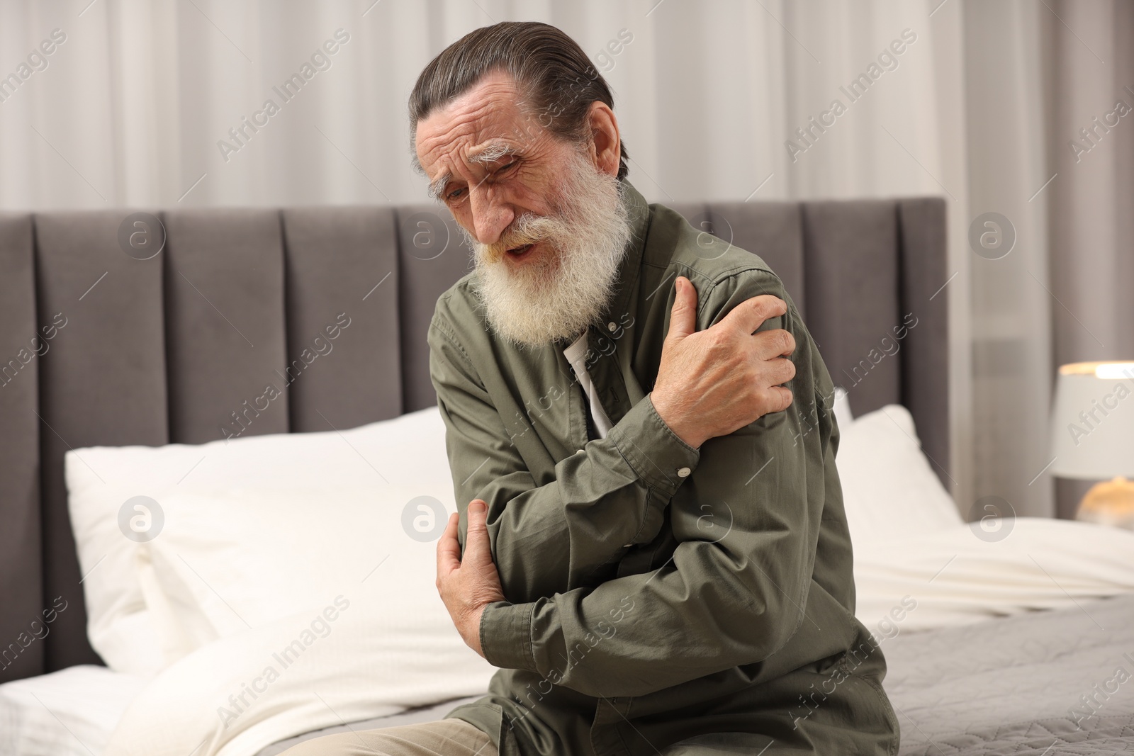 Photo of Senior man suffering from pain in arms on bed at home. Rheumatism symptom