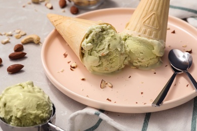 Photo of Delicious pistachio ice cream in wafer cones with chopped nuts on light table, closeup