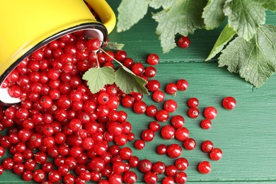 Photo of Many ripe red currants, mug and leaves on green wooden table