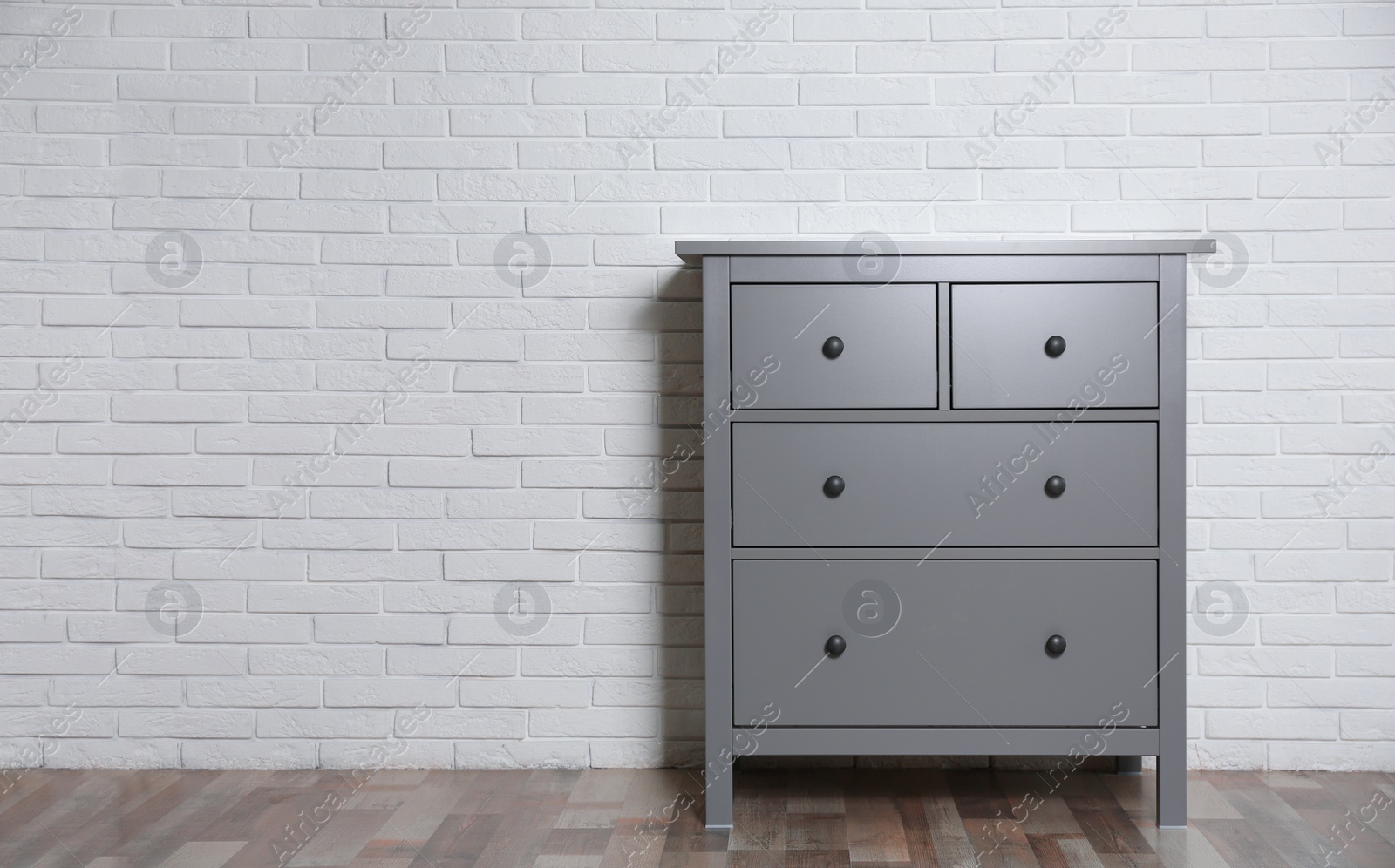 Photo of Grey chest of drawers near white brick wall indoors. Space for text