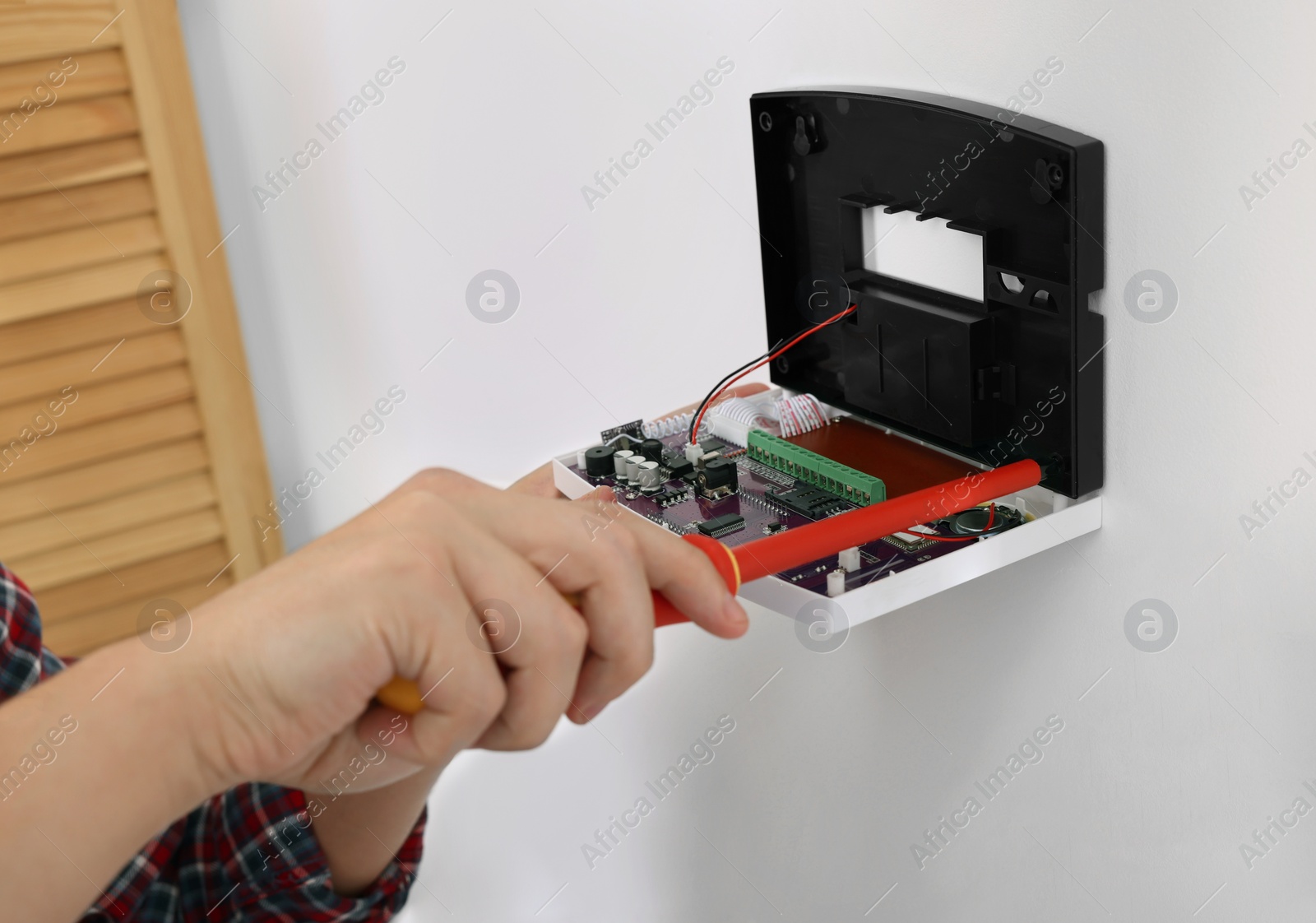 Photo of Man installing home security alarm system on white wall indoors, closeup