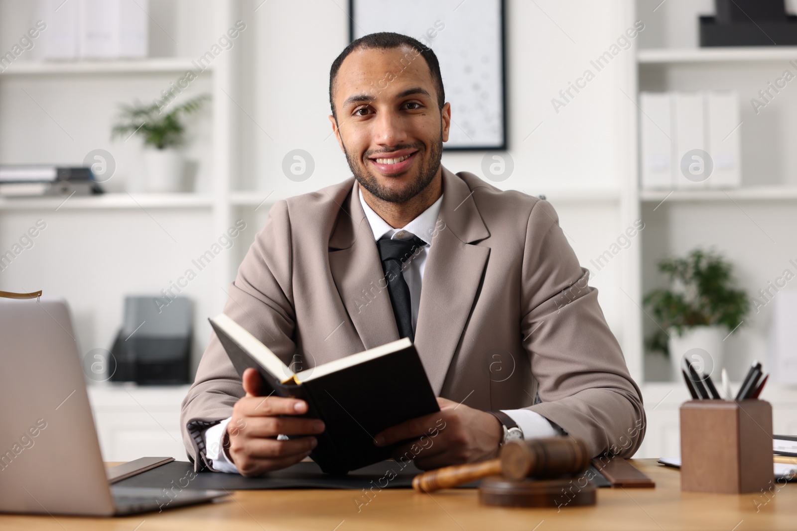 Photo of Smiling lawyer with book at table in office